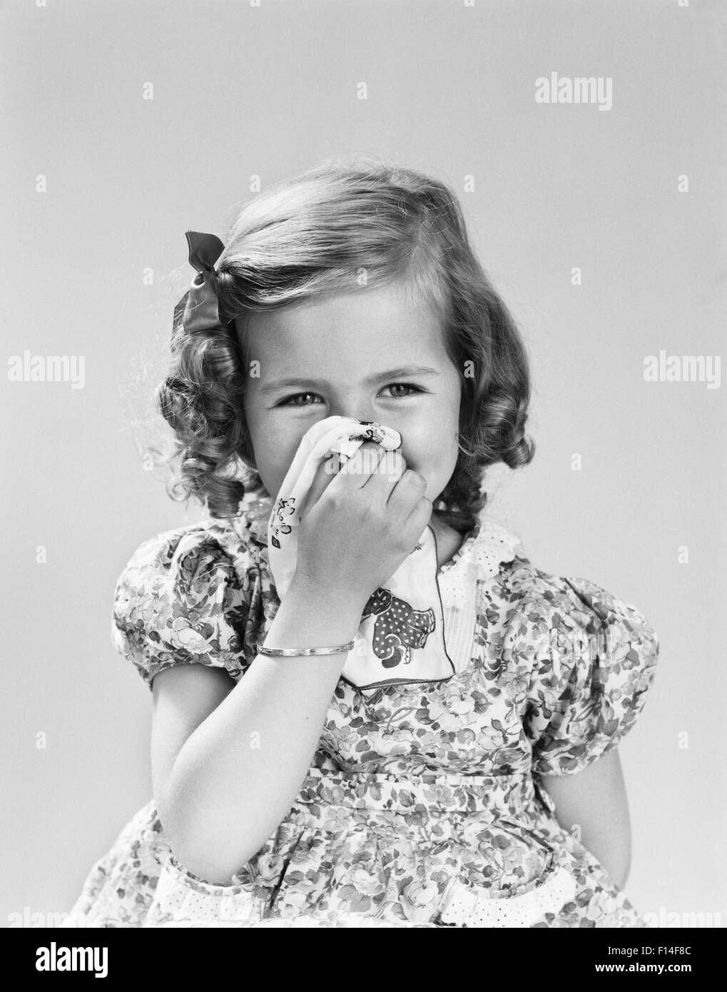 1940s LITTLE GIRL BLOWING HER NOSE WITH CLOTH HANDKERCHIEF Stock Photo