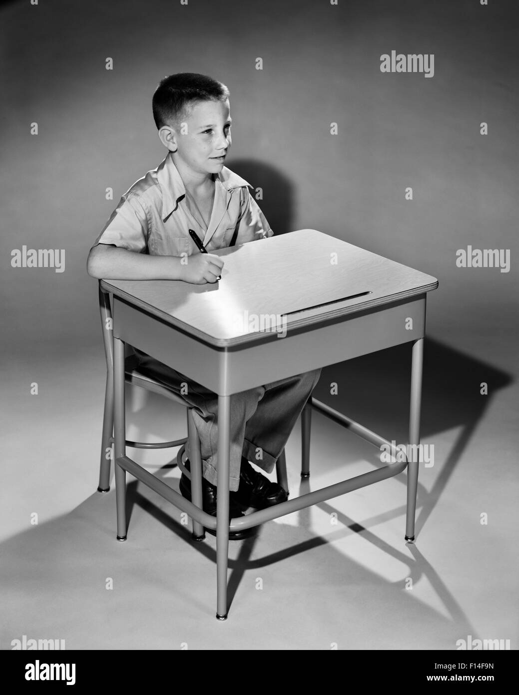 1950s YOUNG BOY HOLDING PEN SITTING AT ELEMENTARY SCHOOL DESK Stock Photo
