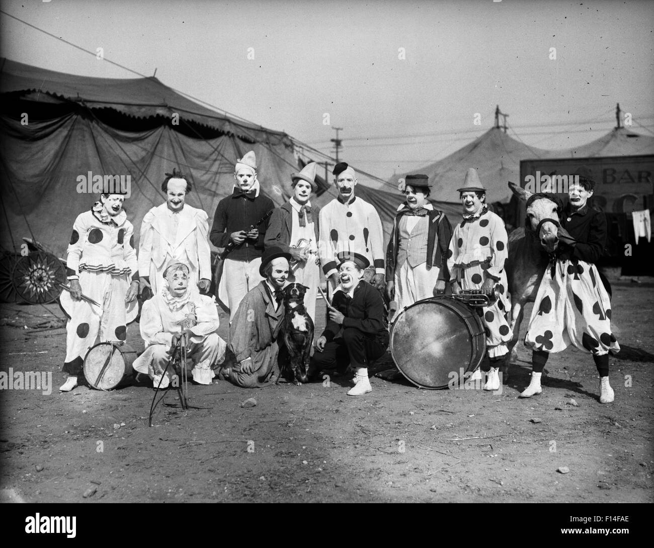 1930s GROUP PORTRAIT OF CLOWNS CIRCUS PERFORMERS POSING WITH ANIMALS AND MUSICAL INSTRUMENTS IN FRONT OF TENTS Stock Photo