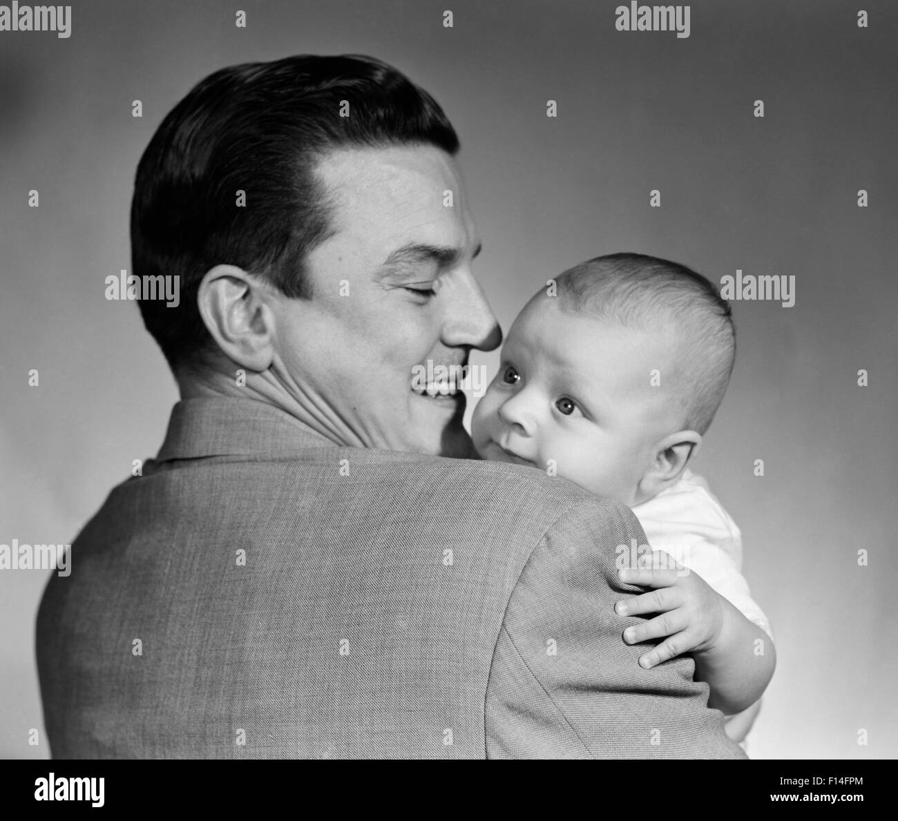 1950s PROUD SMILING MAN FATHER BACK TOWARD CAMERA HOLDING BABY SON FACE TO CAMERA Stock Photo