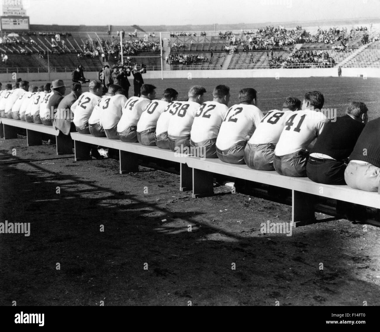 1940s HIGH SCHOOL OR COLLEGIATE FOOTBALL TEAMS FROM BEHIND ALL SITTING ON SIDELINE BENCHES Stock Photo