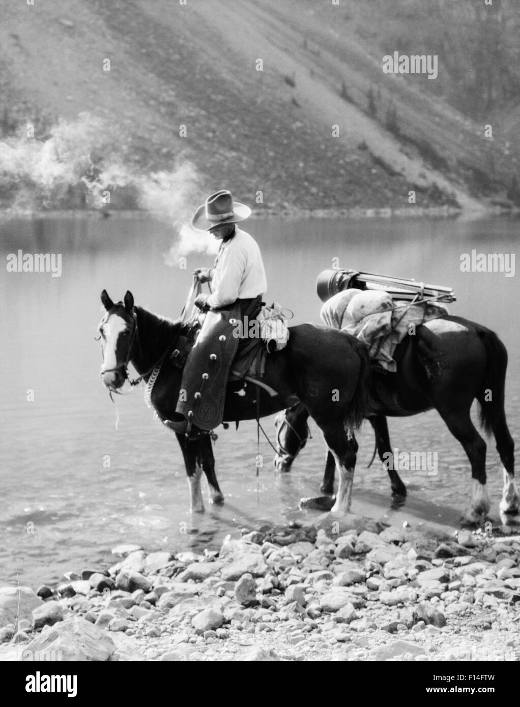 1920s 1930s MAN COWBOY ON HORSE WITH PACK HORSE BY MORAINE LAKE ALBERTA CANADA Stock Photo