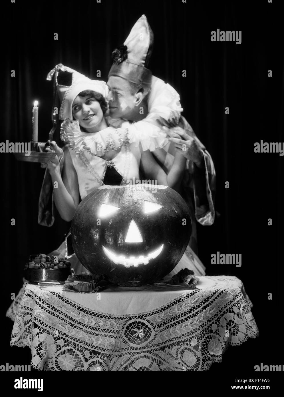 1920s ROMANTIC COUPLE WEARING COSTUMES WITH LARGE CARVED PUMPKIN JACK-O-LANTERN ON TABLE Stock Photo