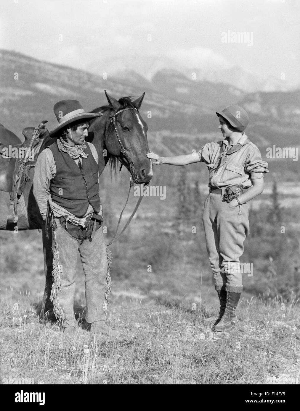 1920s OUTDOOR WOMAN TALKING WITH NATIVE AMERICAN STONEY SIOUX INDIAN WESTERN TRAIL GUIDE MAN AND HIS HORSE ALBERTA CANADA Stock Photo