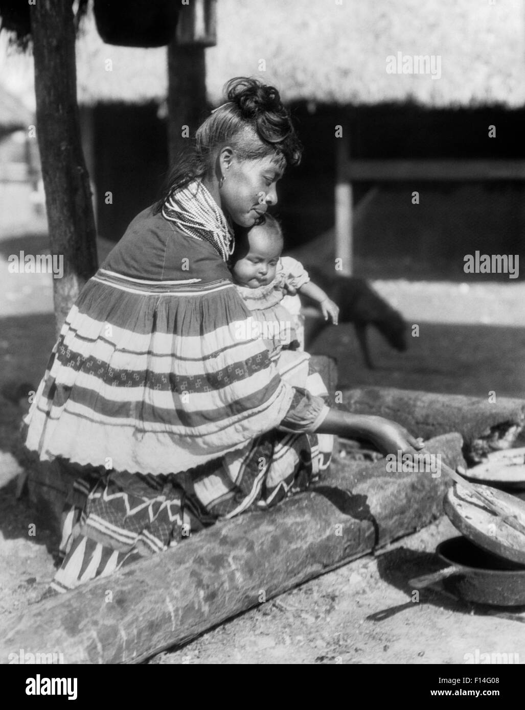 1920s NATIVE AMERICAN SEMINOLE WOMAN HOLDING BABY AND COOKING FLORIDA USA Stock Photo