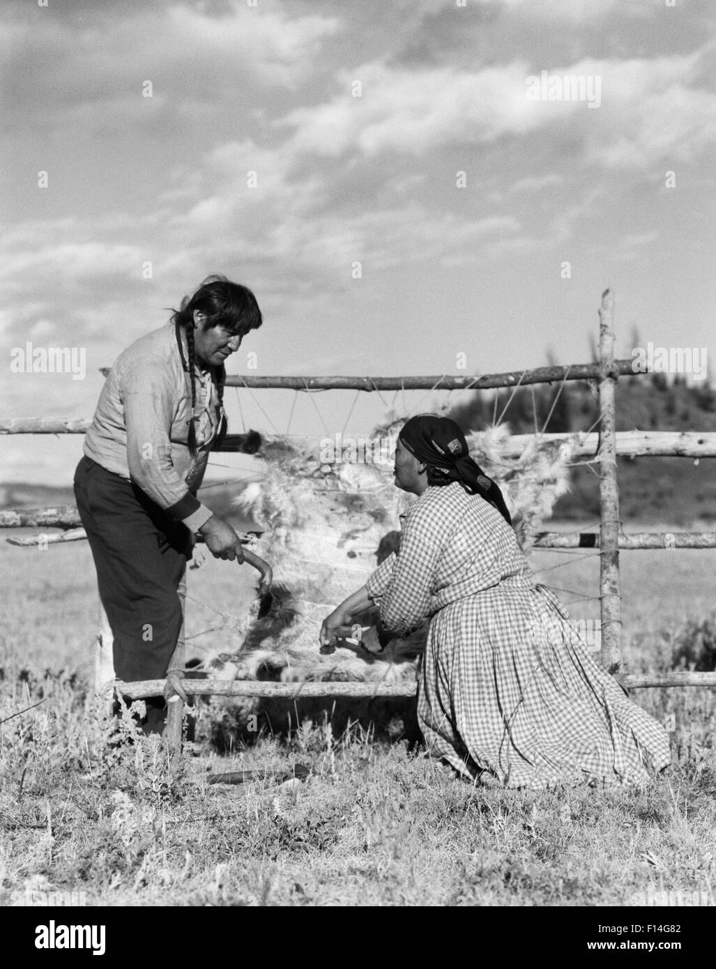 1920s NATIVE AMERICAN COUPLE MAN WOMAN TREATING ANIMAL HIDE SKIN STONEY SIOUX ALBERTA CANADA Stock Photo