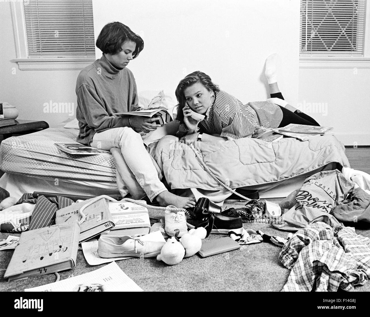 1980s TWO TEENAGE AFRICAN AMERICAN GIRLS IN CLUTTERED BEDROOM ONE TALKING ON THE PHONE ONE READING MAGAZINE Stock Photo