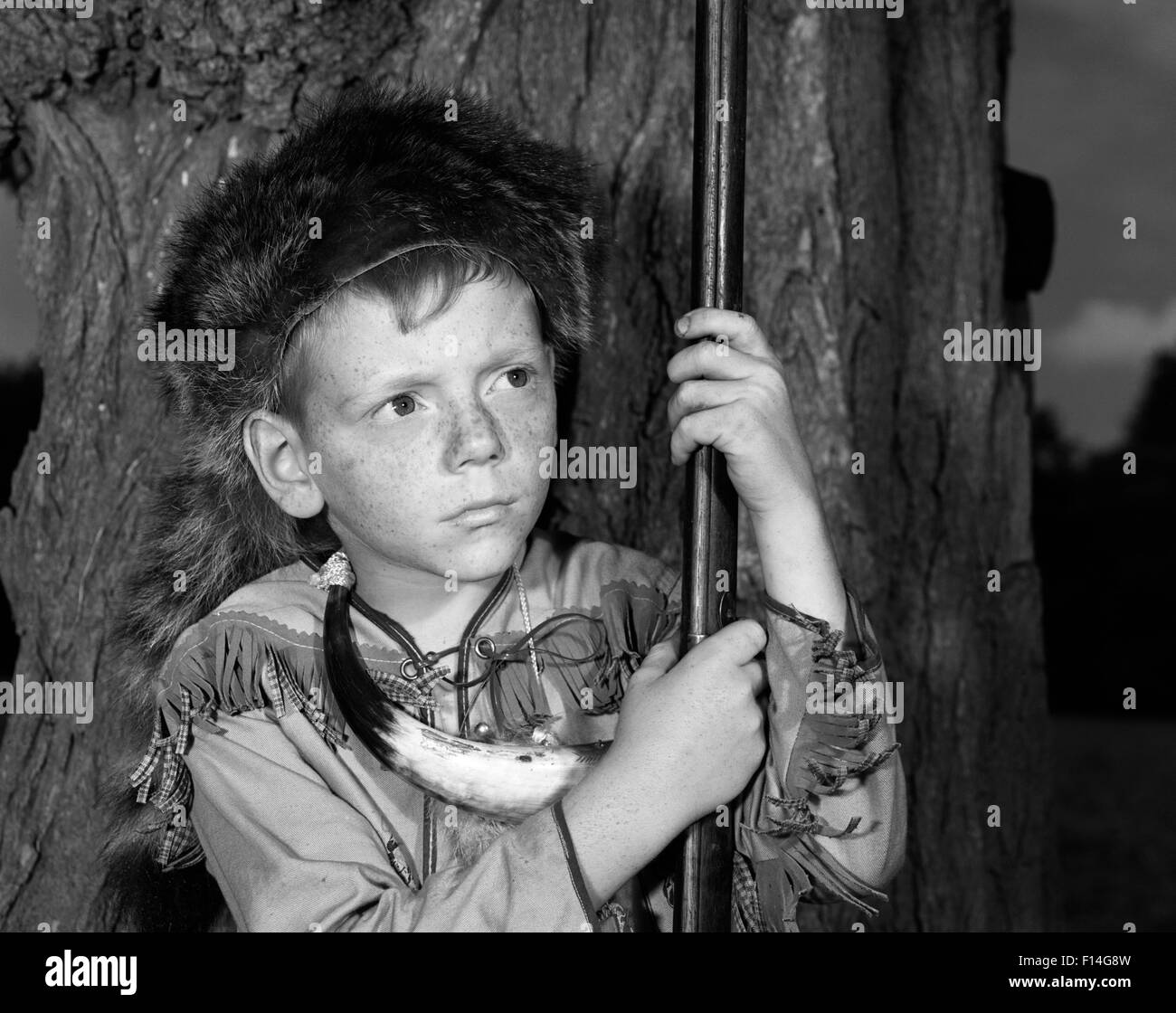 1950s BOY WEARING RACCOON SKIN HAT FRINGED WESTERN STYLE JACKET WITH POWDER HORN AND ANTIQUE