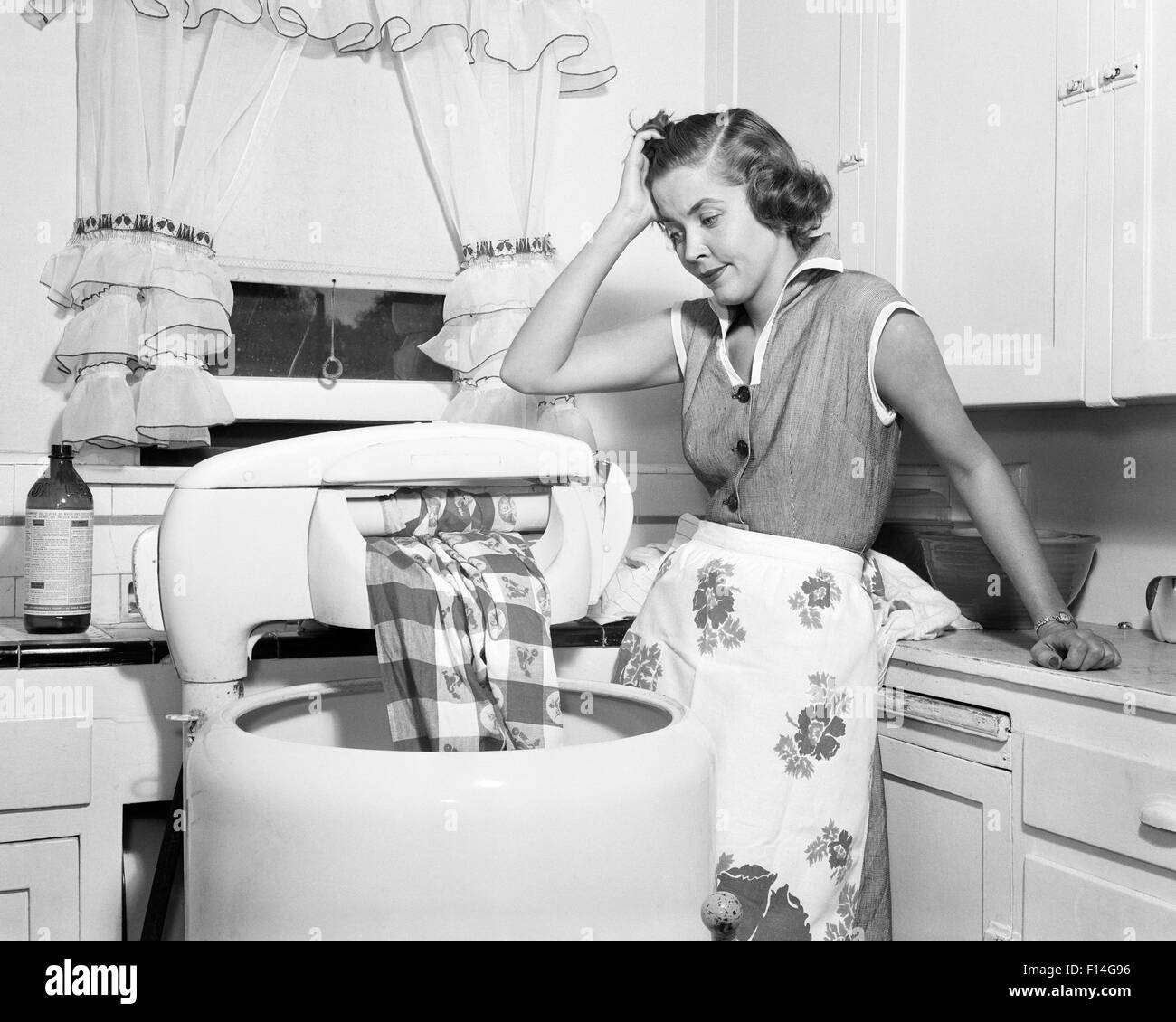 1950s FRUSTRATED HOUSEWIFE WITH JAMMED WRINGER ON CLOTHES WASHING MACHINE IN KITCHEN Stock Photo
