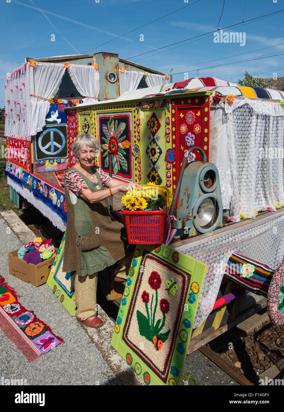 Peace activist and co-initiator Christa Senberg stands in front of an old diesel locomotive covered by a colourful knitted garment at a hand car depot in Zossen, Germany, 26 August 2015. Held for the second time at this location is the movement 'Knitting for Peace'. After a huge success in 2013, where many dedicated knitting and crochet fans from all over Germany and neighbouring countries turned the diesel locomotives into symbols for piece, there is now a sequel event.  Under the slogan 'Make love, not war' Visitors and friends of small trains have been invited to submit their colourful knit Stock Photo
