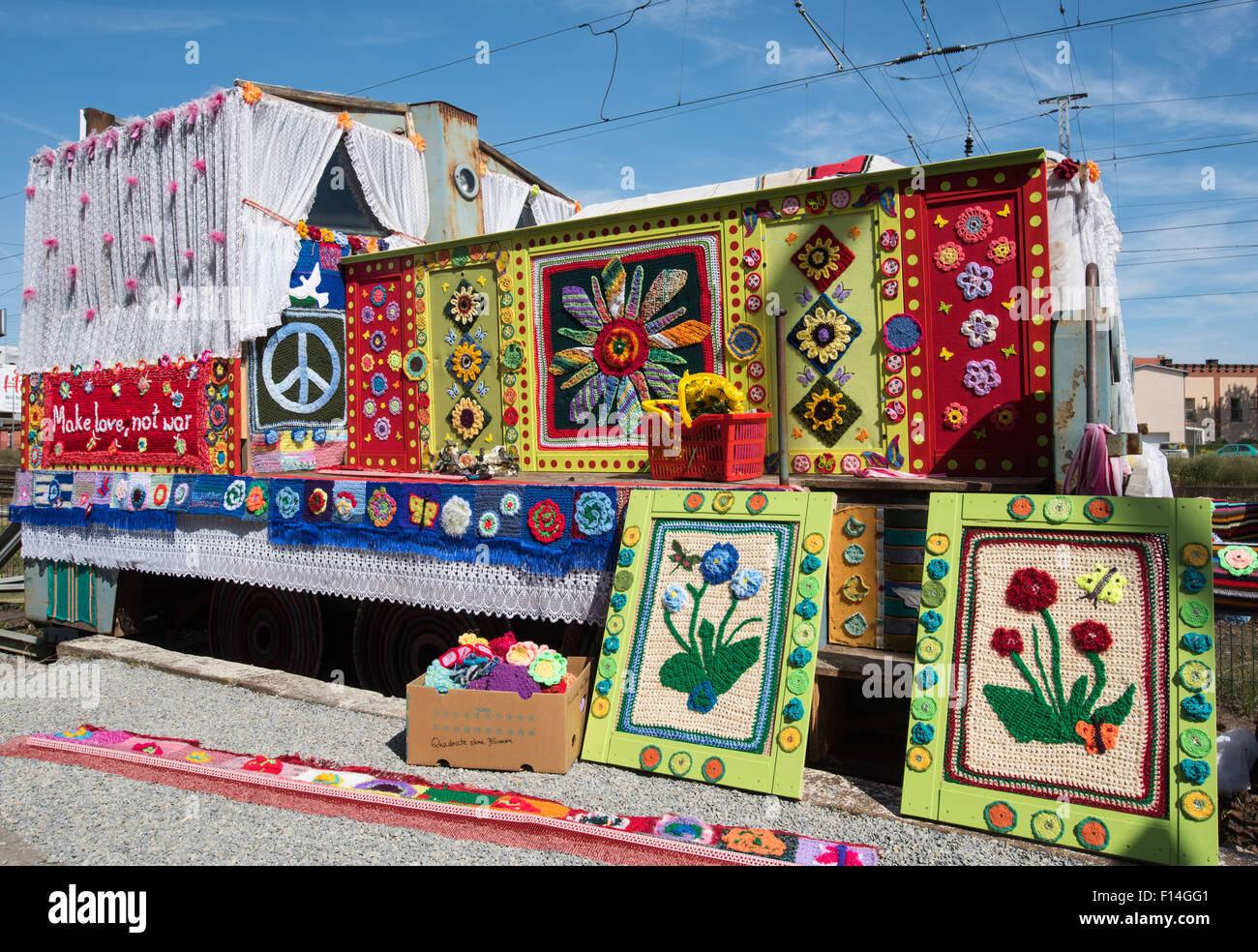 Peace activists Christa Senberg stands with an old diesel locomotive covered by a colourful knitted garment at a hand car depot in Zossen, Germany, 26 August 2015. Held for the second time at this location is the movement 'Knitting for Peace'. After a huge success in 2013, where many dedicated knitting and crochet fans from all over Germany and neighbouring countries turned the diesel locomotives into symbols for piece, there is now a sequel event.  Under the slogan 'Make love, not war' Visitors and friends of small trains have been invited to submit their colourful knitwear and crochet via so Stock Photo