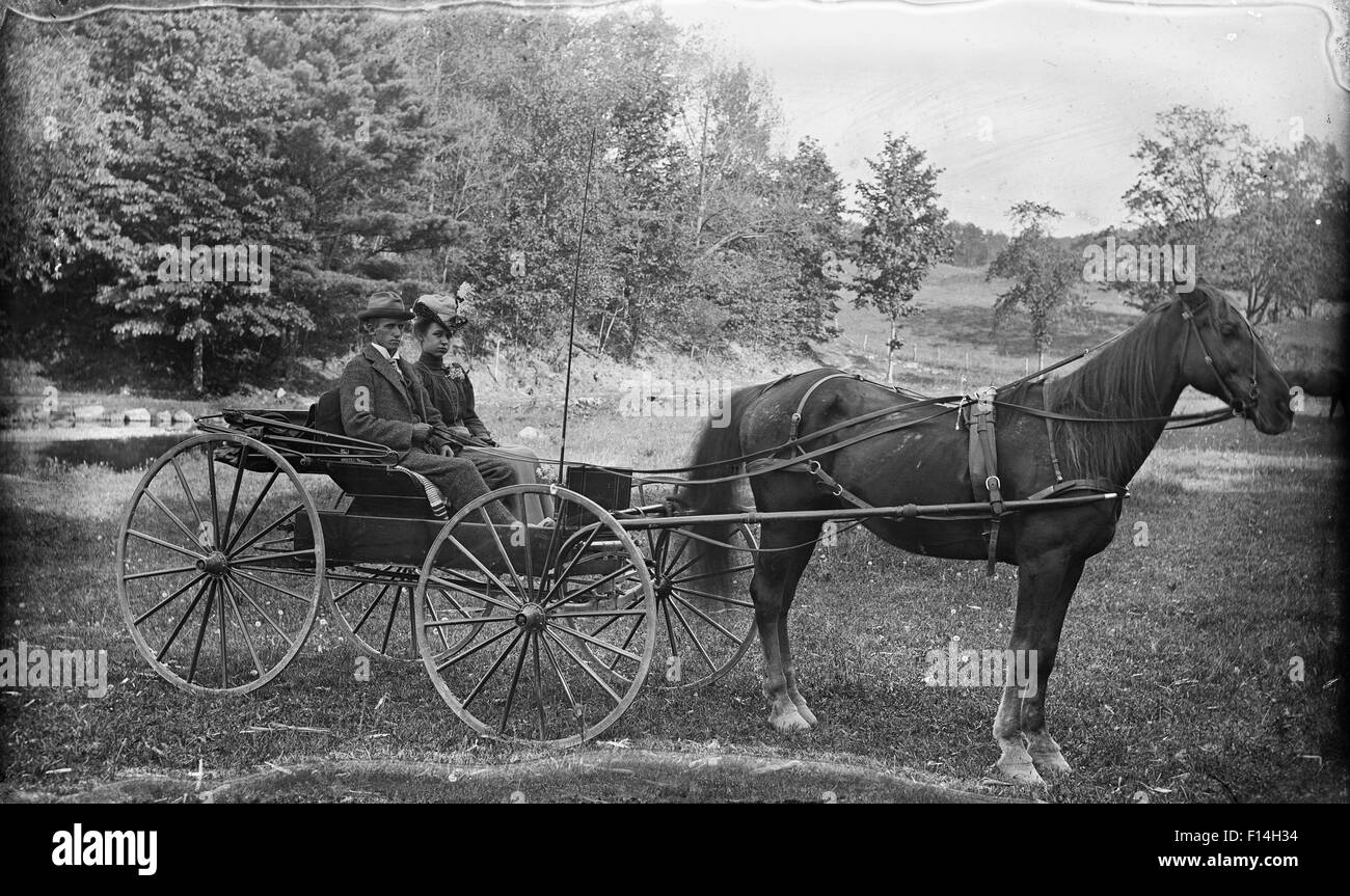 1890 1890s TURN OF THE 20TH CENTURY COUPLE MAN WOMAN RIDING IN HORSE DRAWN BUGGY CARRIAGE LOOKING AT CAMERA Stock Photo