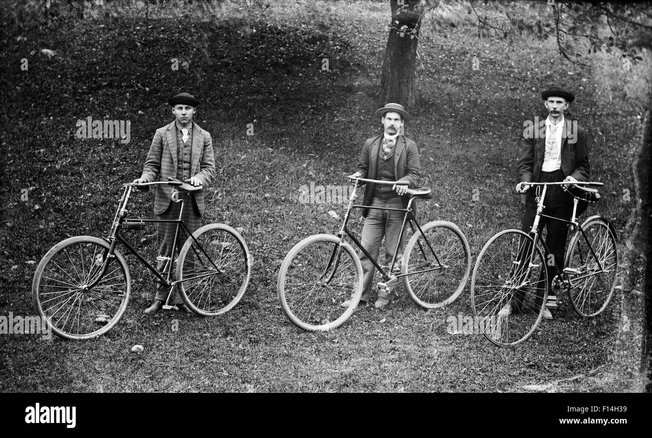 1900 1900s THREE TURN OF THE 20TH CENTURY MEN POSING STANDING BY BICYCLES LOOKING AT CAMERA Stock Photo
