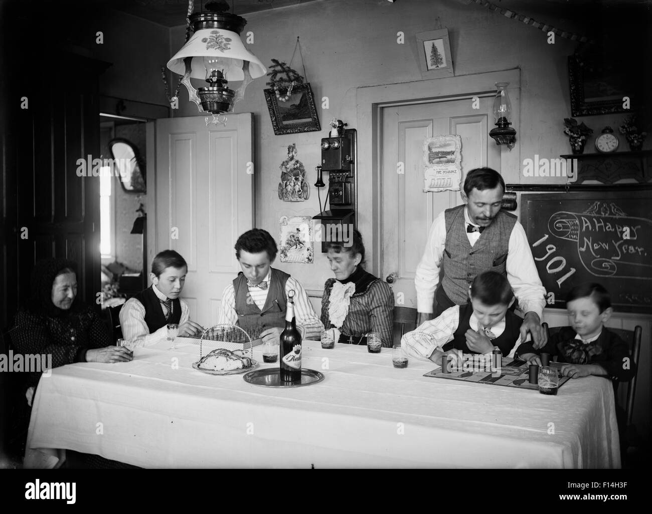 1900s 1901 TURN OF 20 CENTURY FAMILY THREE GENERATIONS AT KITCHEN TABLE  NEW YEARS CELEBRATION Stock Photo