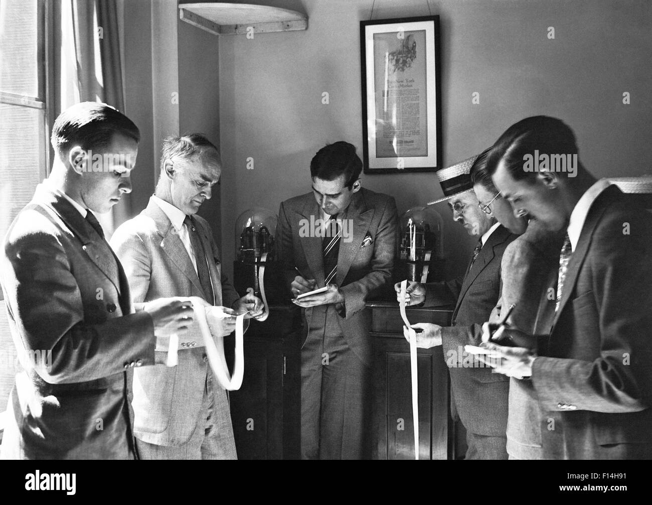 1930s SIX ENGROSSED INVESTORS AND STOCK BROKERS READING PAPER TICKER TAPE INVENTED IN 1867 BY EDWARD CALAHAN NEW YORK CITY USA Stock Photo