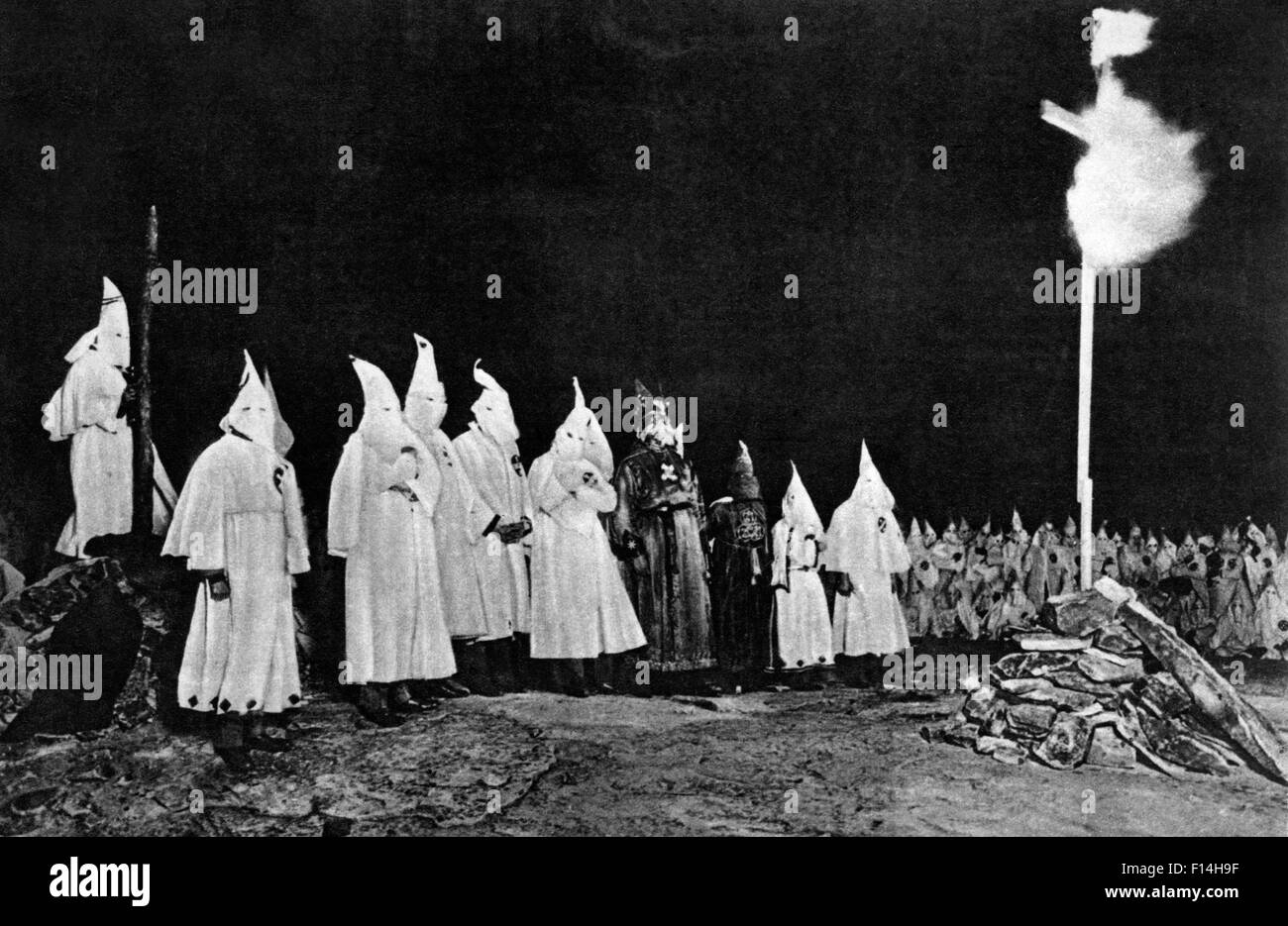 1930s KU KLUX KLAN KKK GATHERING WITH IMPERIAL WIZARD OPPOSITE A FIERY BURNING CROSS IN RURAL GEORGIA USA Stock Photo