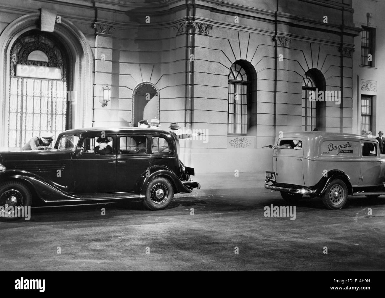 1930s MOVIE STILL OF NIGHTTIME SHOOTOUT BETWEEN GANGSTERS IN A PARKED CAR AND A PASSING PANEL TRUCK Stock Photo