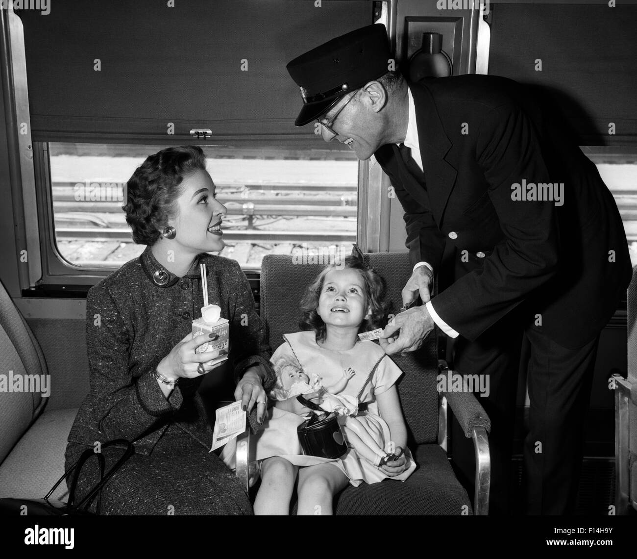 1950s MOTHER AND DAUGHTER ON TRAIN WITH CONDUCTOR PUNCHING THEIR TICKET Stock Photo