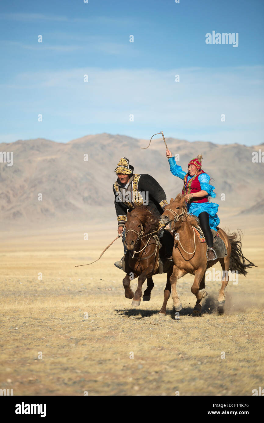 Eagle hunter woman whipping man on slow Mongolian horse to try to slow him down during game at the Eagle hunter's festival. She is on a faster horse but if he wins the game he is entitled to a kiss. Eagle Hunters Festival, near Sagsai, Bayan-Ulgii Aymag, Stock Photo
