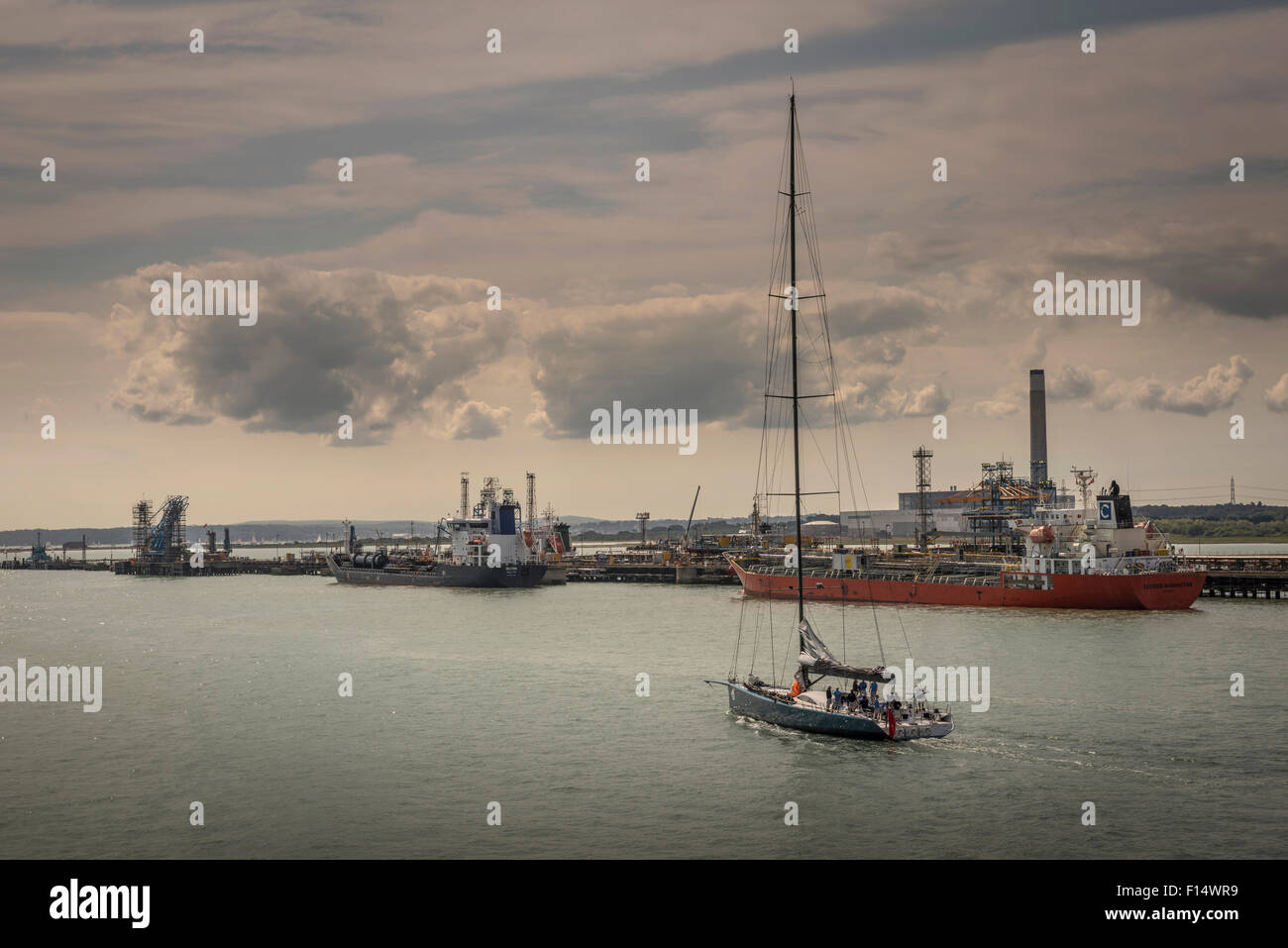 A sailing yacht passing oil tankers docked at Fawley Oil Refinery near Southampton, Hampshire, UK Stock Photo