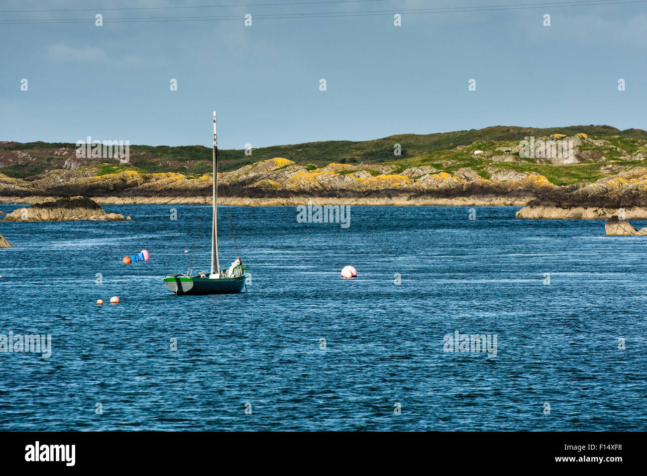 Summer coastal scene of rocky shoreline with moored sailing boat in