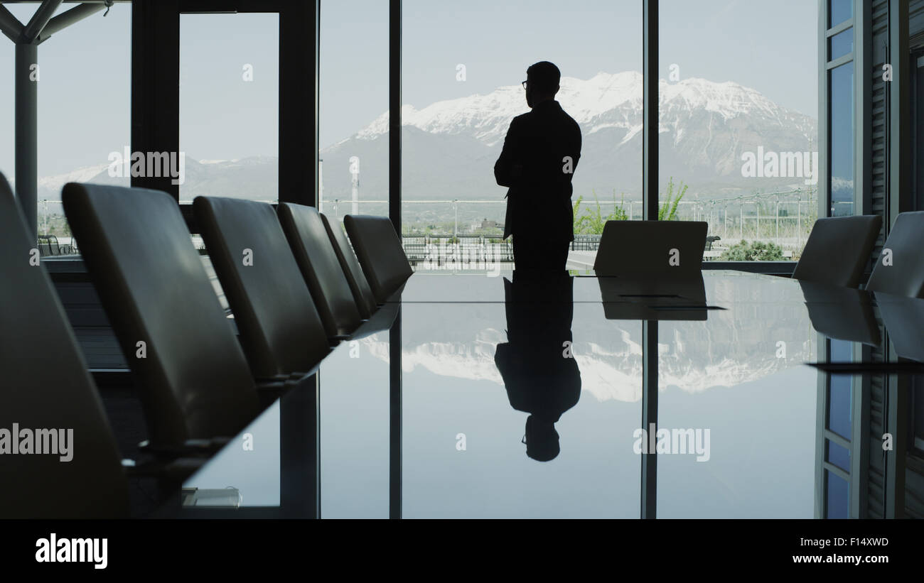 Silhouette of businessman reflecting in conference table and looking at scenic view from office window Stock Photo