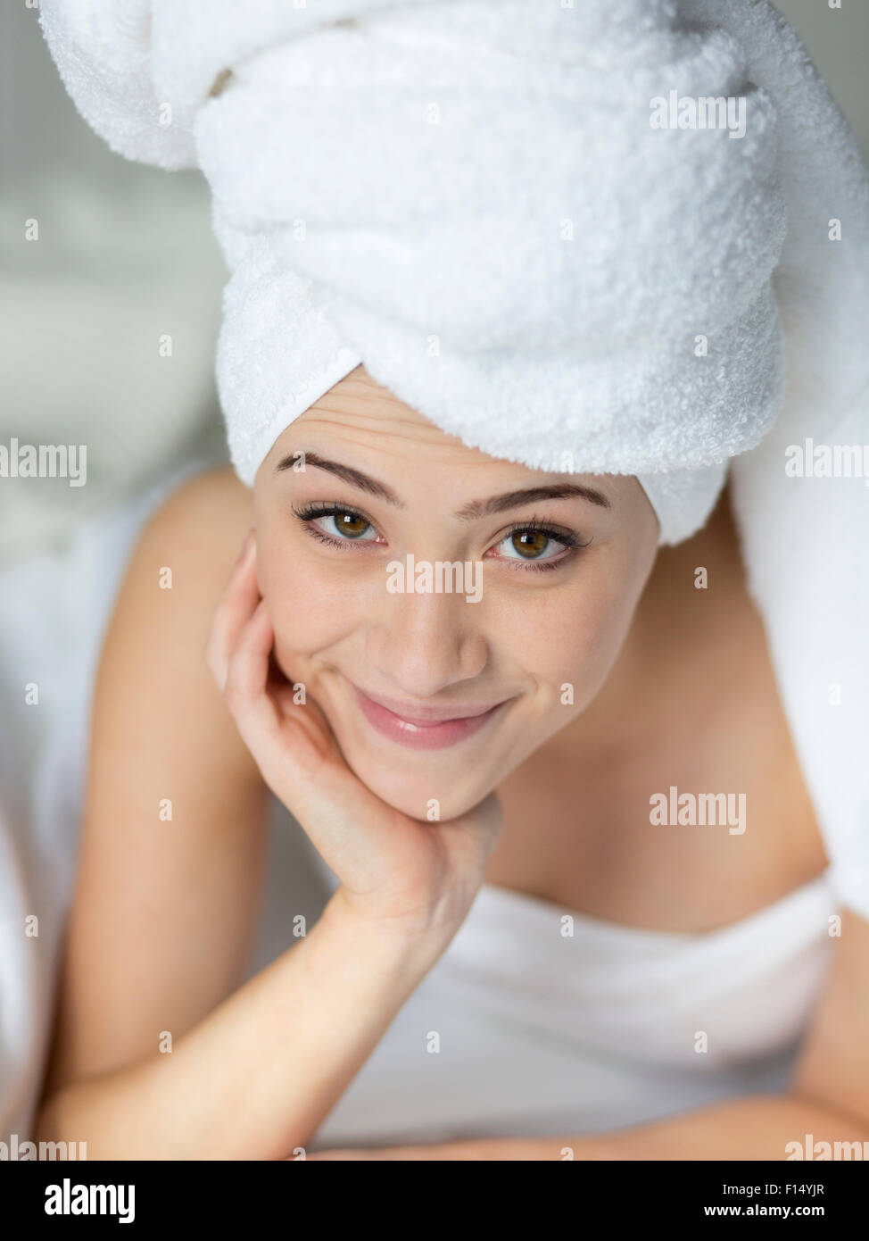 Smiling woman with head wrapped in towel and hand on chin Stock Photo