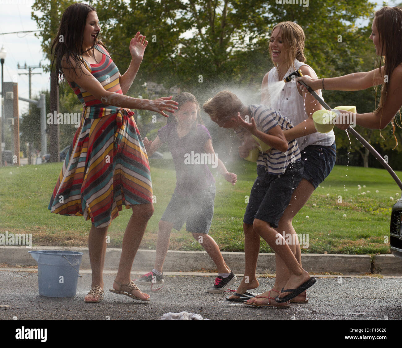 Wet laughing family playing in spraying water hose in park Stock Photo ...