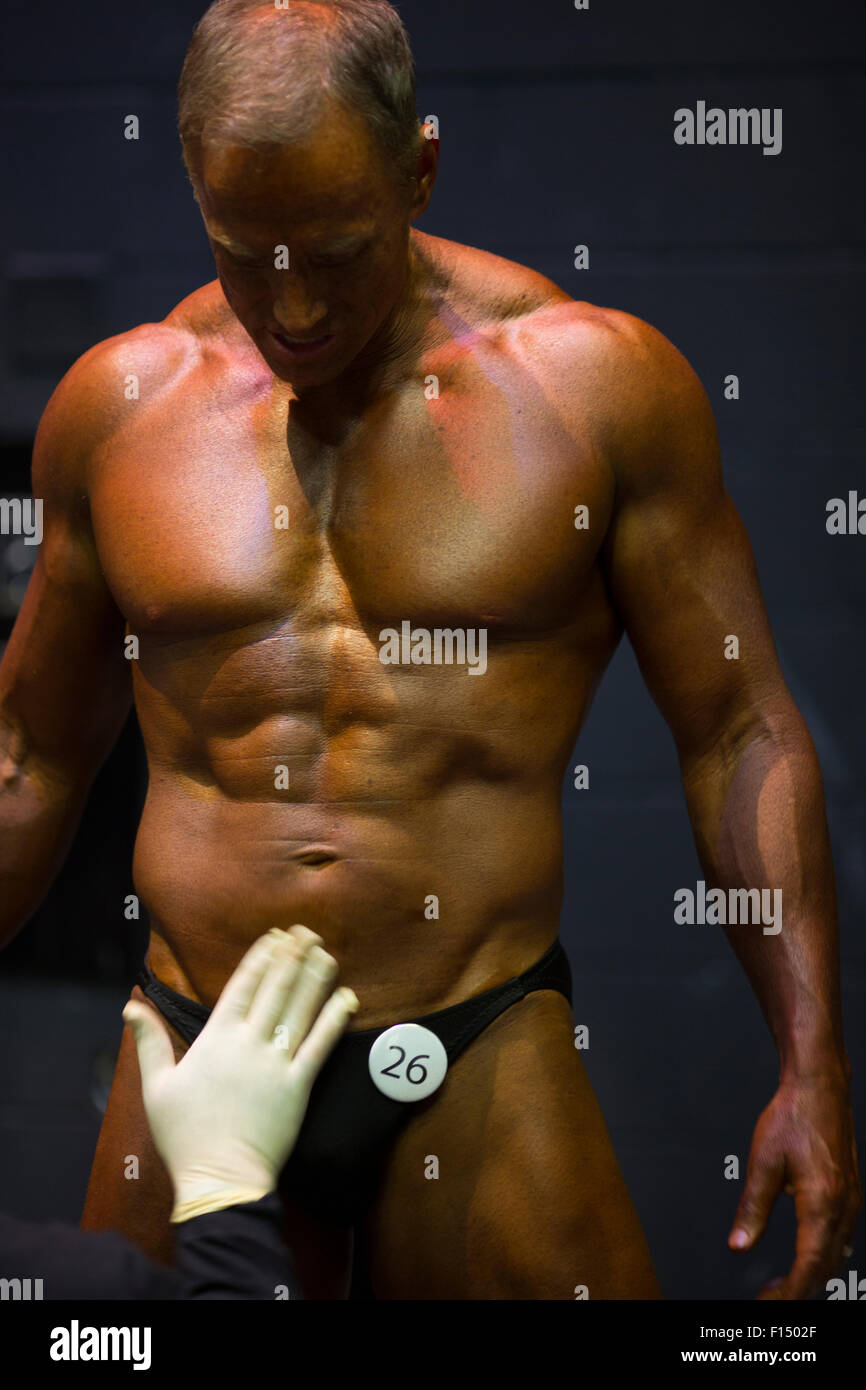 Stylist rubbing tanning lotion on bodybuilder competitor preparing for performance Stock Photo
