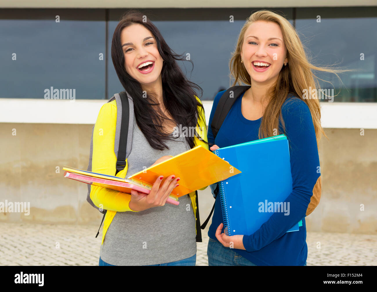 Two beautiful and happy teenage students showing something on the books ...