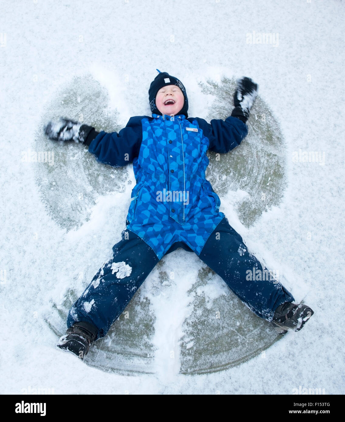 Child lying in the snow creating snow angel, Norway, January 2014. Model released. Stock Photo