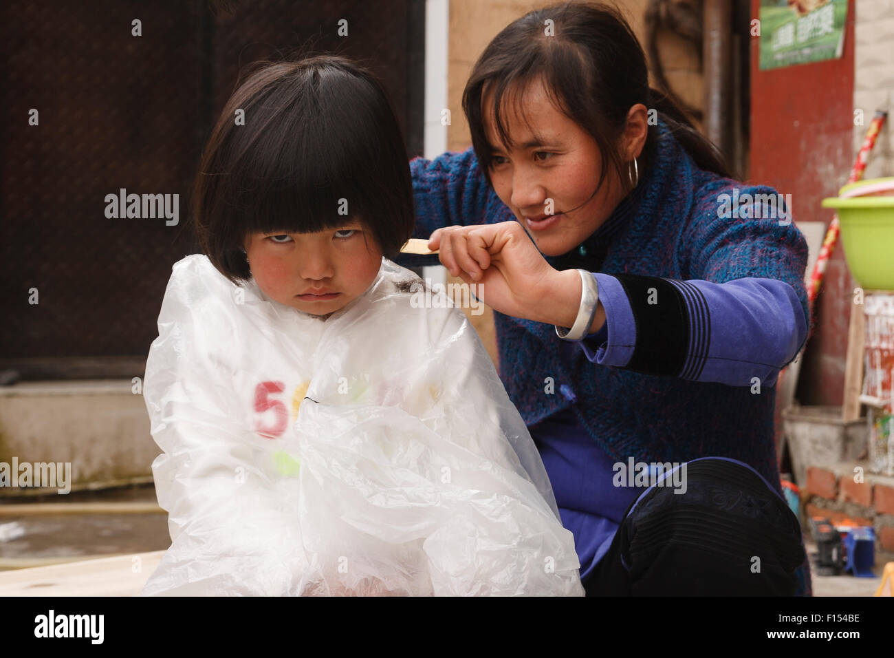 5 year old Hani Chinese girl sulking having her hair cut in street Stock Photo