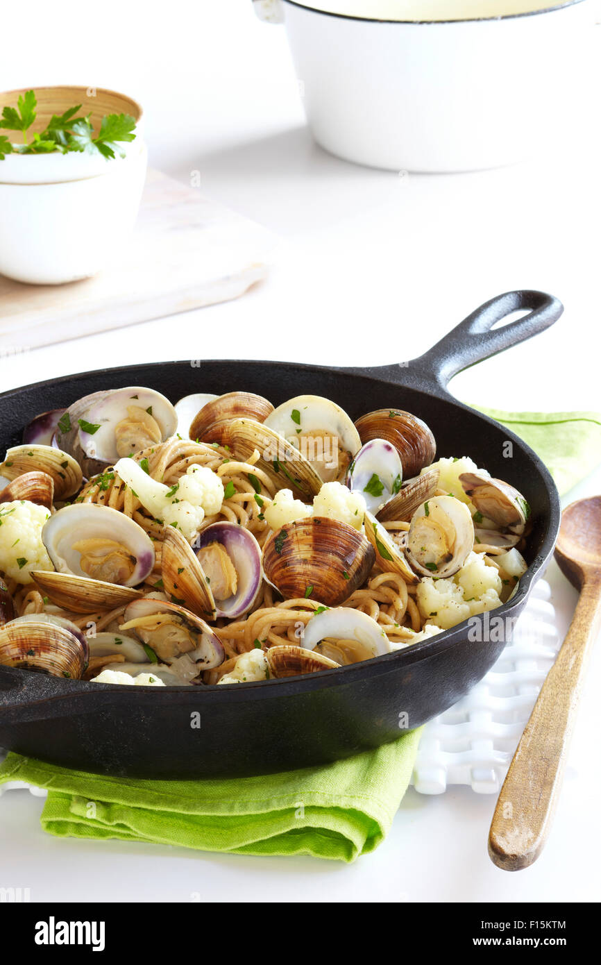 Cast iron skillet with whole wheat pasta, cauliflower and clams on a green napkin with a wooden spoon, studio shot Stock Photo