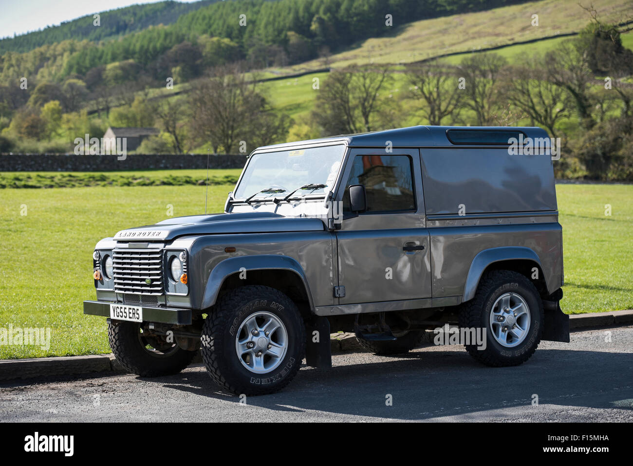 Clean, shiny, grey, hard top Land Rover Defender (iconic, rugged 4x4 vehicle) parked in sunny spot on a Yorkshire Dales road - Burnsall, England, UK. Stock Photo
