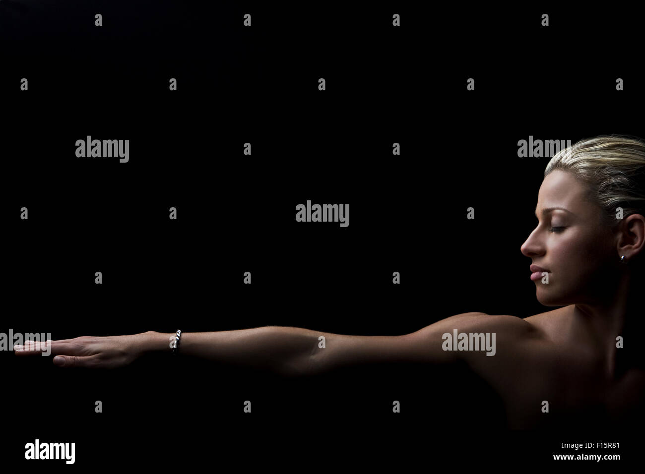 dramatic studio portrait of fit blonde female athlete eyes closed with one outstretched arm across bottom of all black frame Stock Photo