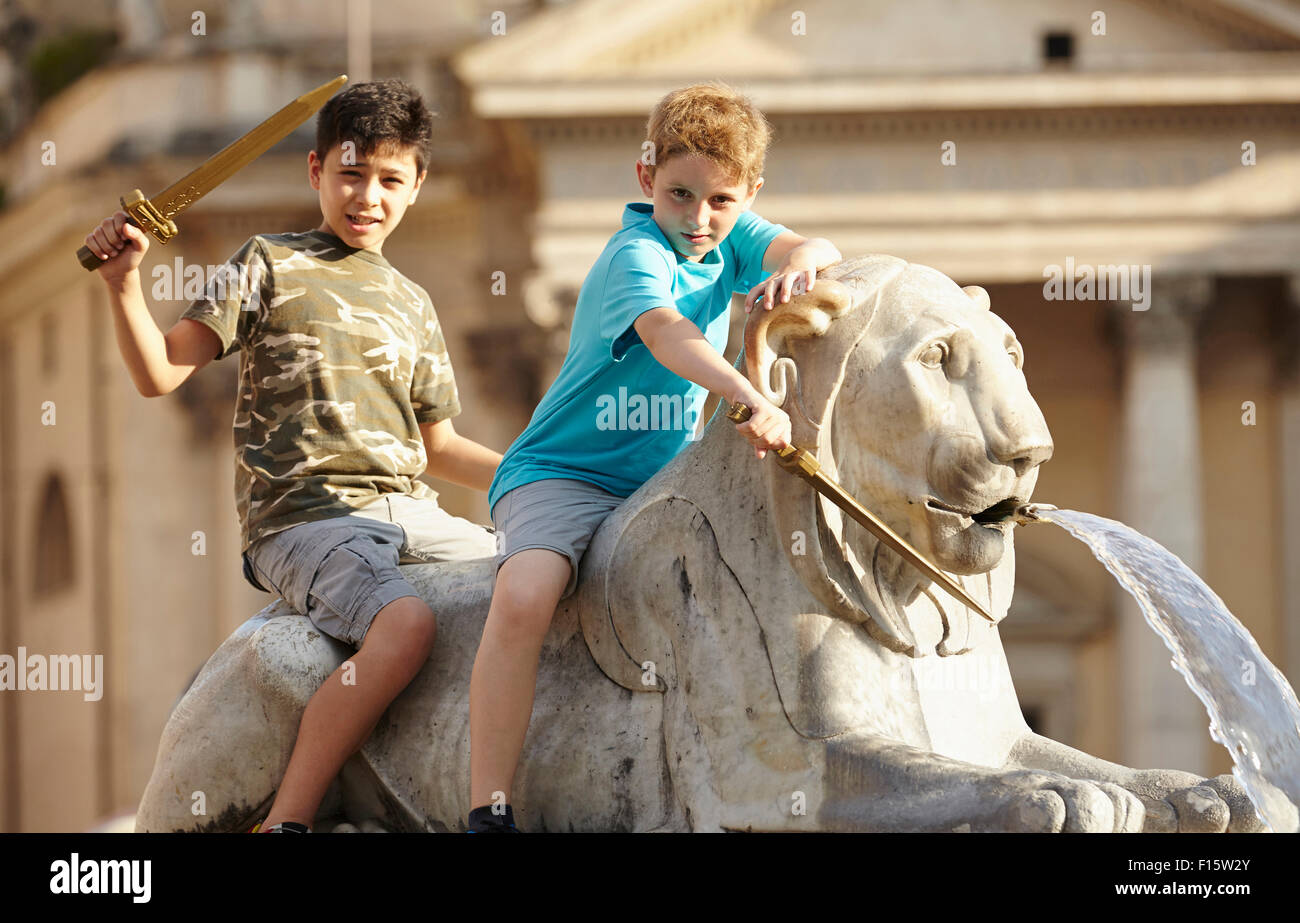 Portrait of two children on lion statue, Fontana dell'Obelisco, Piazza del Popolo (People's Square), summer, Rome, Lazio, Italy Stock Photo
