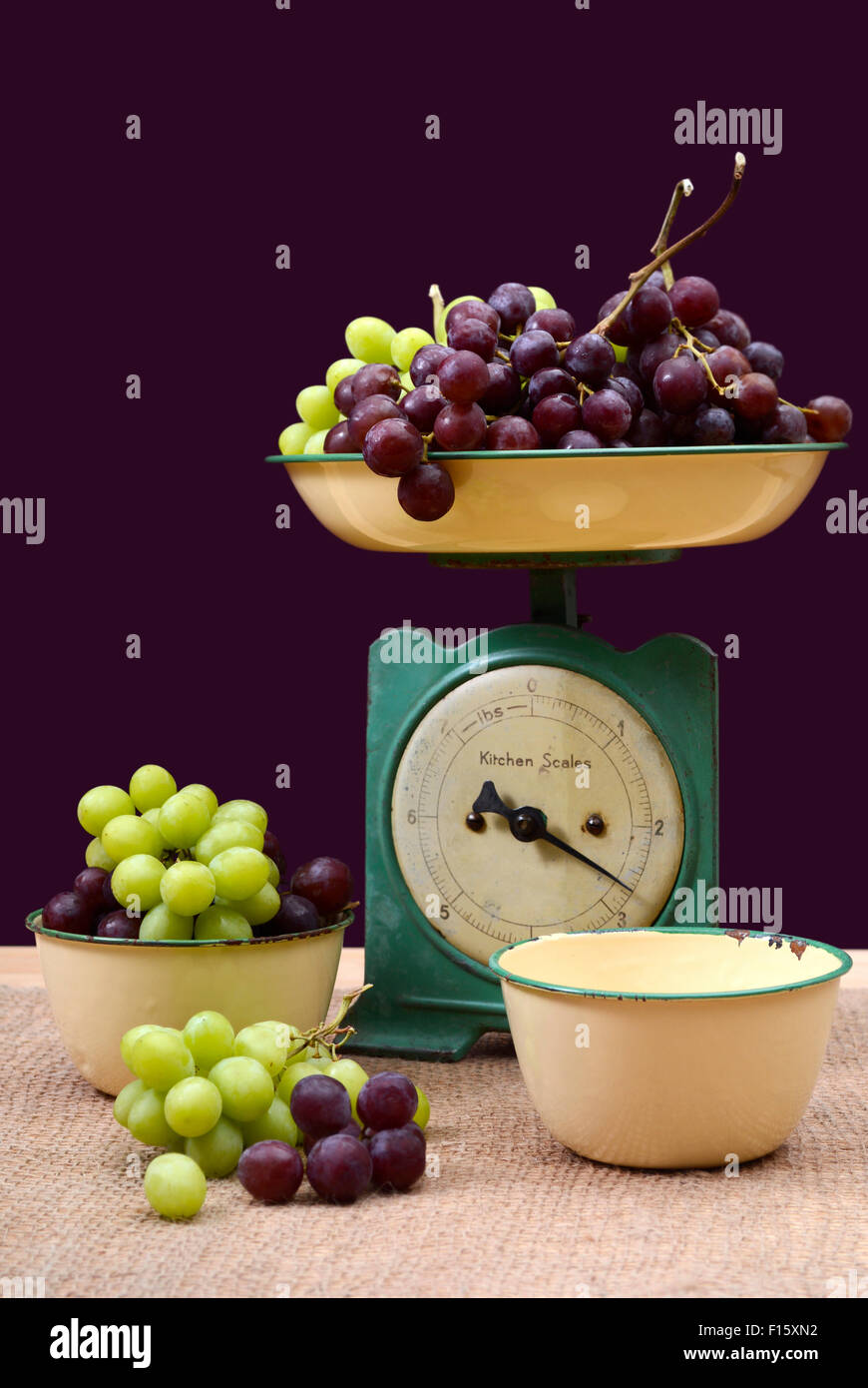 Weighing grapes on vintage scale with old enamel bowls on burlap covered pine table. Stock Photo