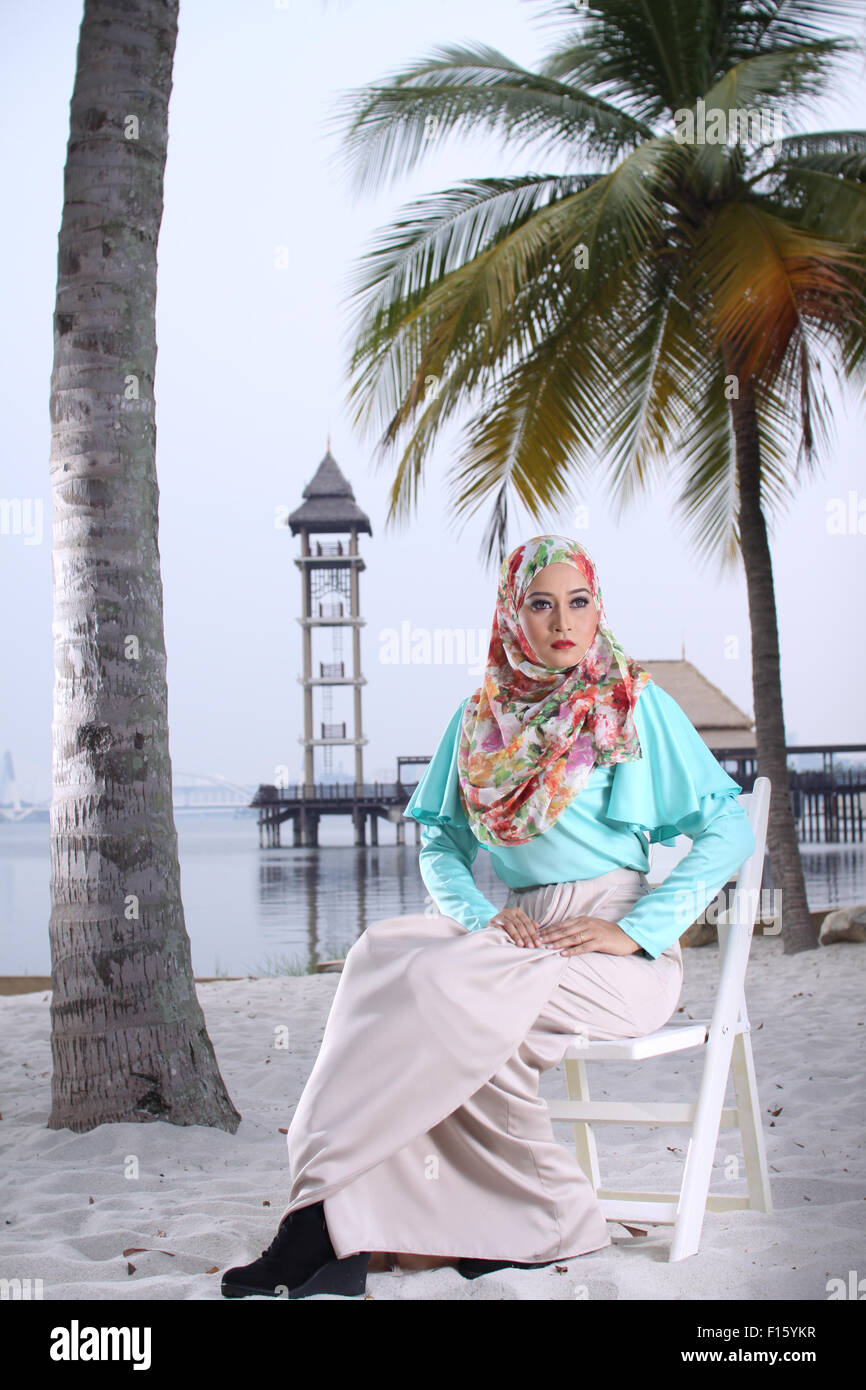 high fashion muslim women sitting at wooden white chair with beach background Stock Photo