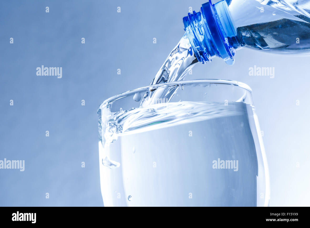 Pouring water from bottle into glass in blue toning Stock Photo - Alamy