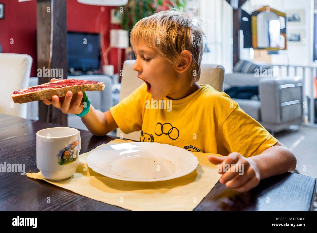 blond boy in yellow jersey eating at the table bread and jam Stock Photo
