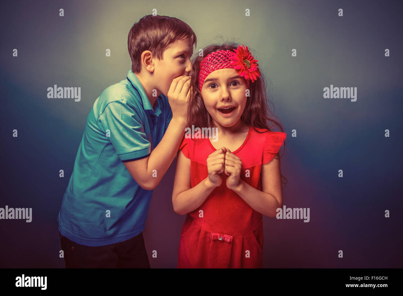 Teen boy whispering in the ear of teen girl on a gray  backgroun Stock Photo