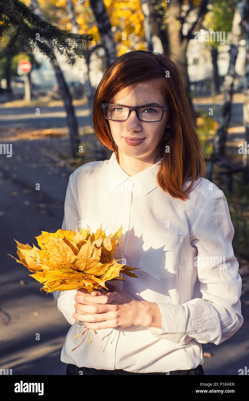 teenage girl in  bright shirt with wisp of maple leaves in bright sunlight in an autumn park Stock Photo