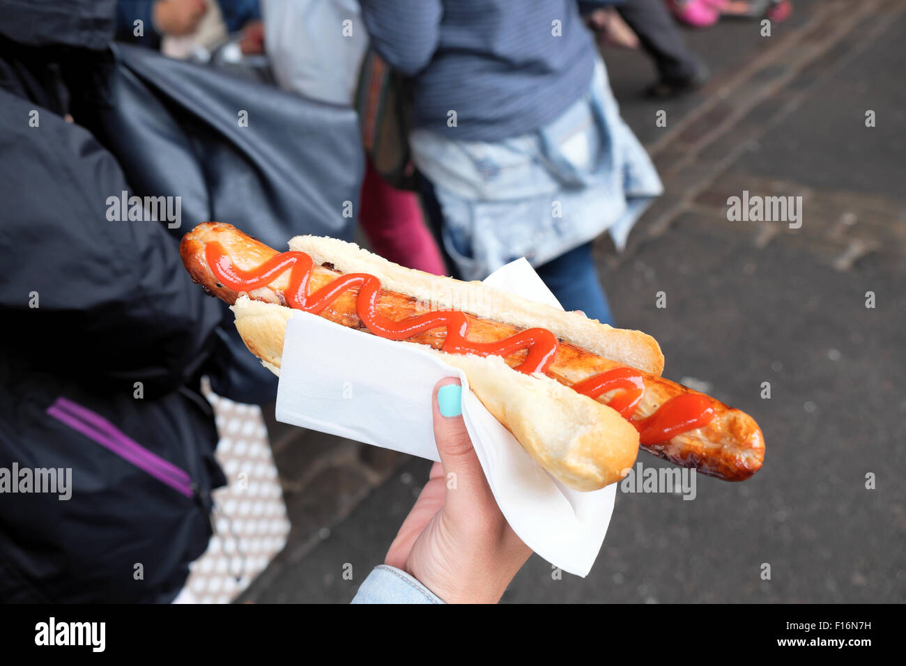 Closeup view of a girl with blue nail varnish eating holding a hotdog in a bun with ketchup in Borough Market South London UK  KATHY DEWITT Stock Photo