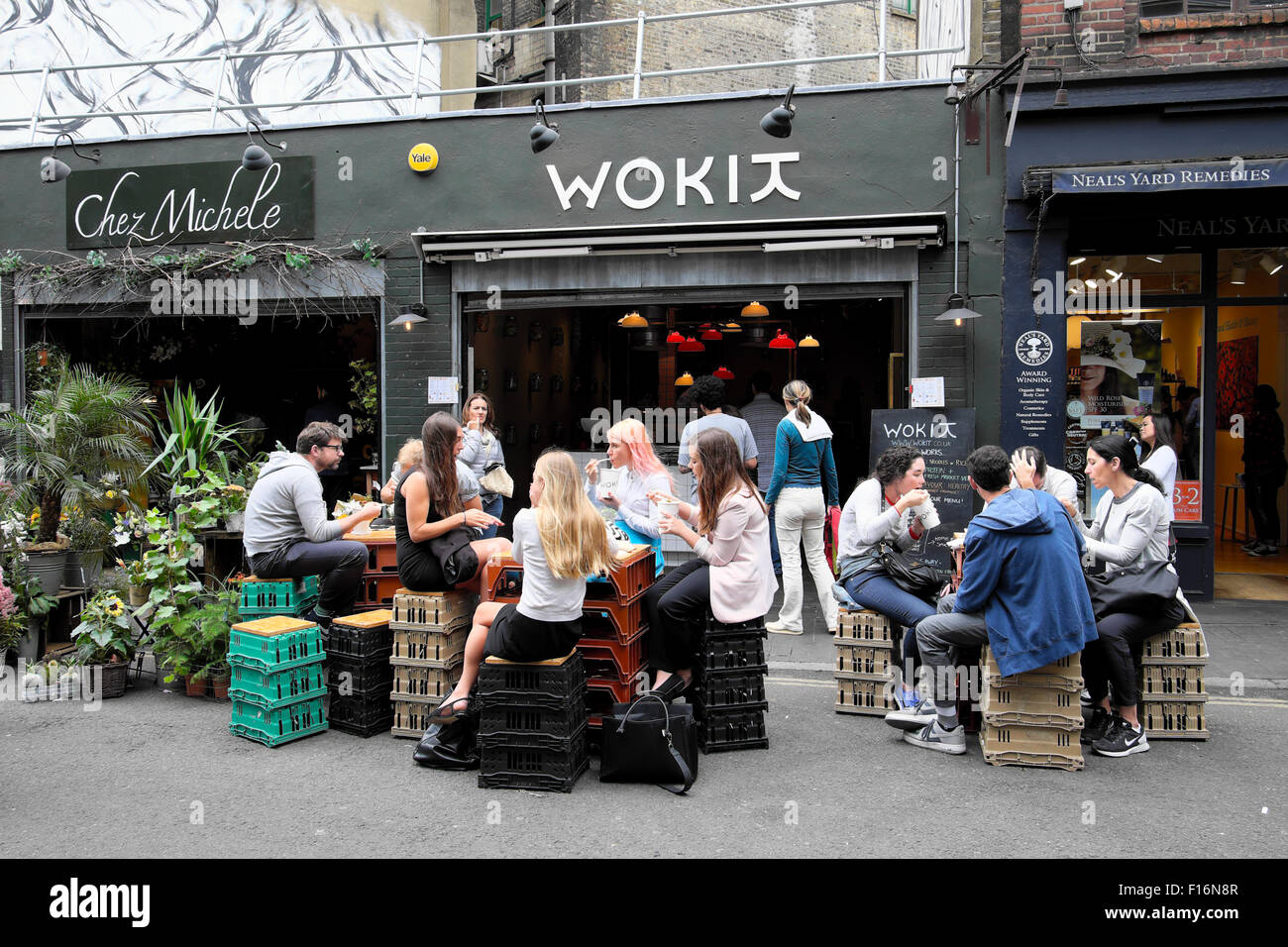 Young people eating and drinking sitting on crates outside WOKIT restaurant at lunchtime in summer near Borough Market in South London UK KATHY DEWITT Stock Photo