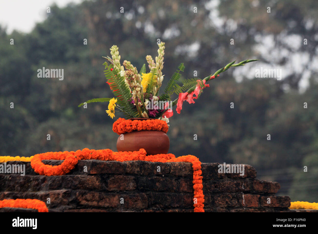 Clay pot of flowers with strands of marigolds along temple wall in