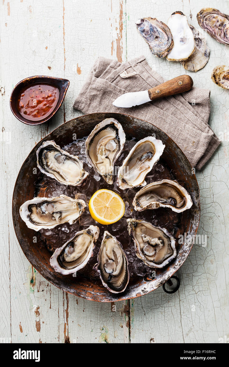 Opened Oysters on metal copper plate on blue wooden background with spicy sauce and oyster knife Stock Photo