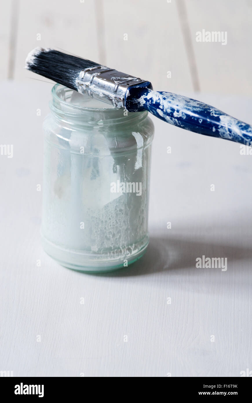 Paintbrush with paint splattered handle balanced on top of a jam jar of white paint - concept still life image of decorating or painting Stock Photo