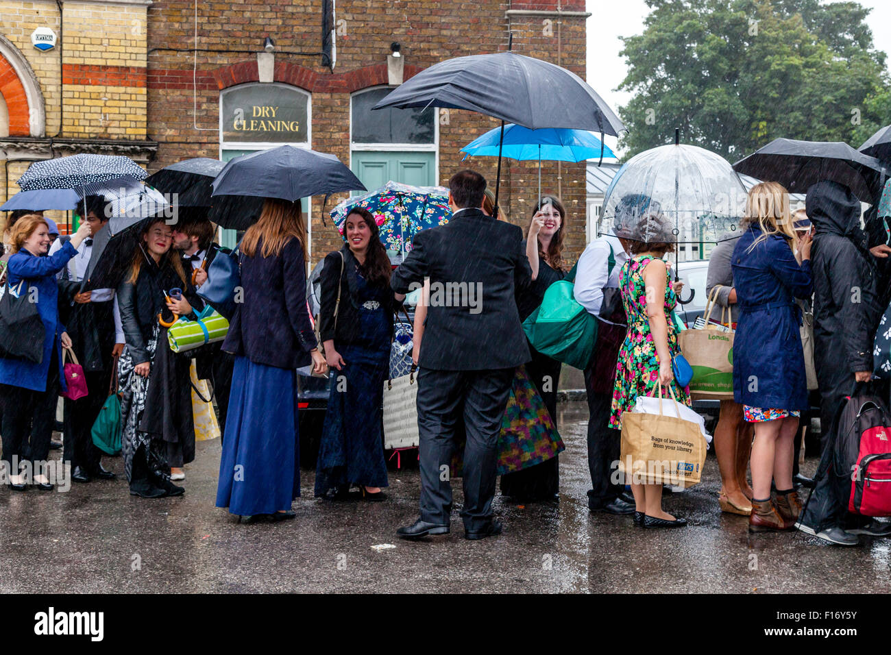 Young Opera Fans Wait In The Pouring Rain At Lewes Station For A Bus Take Them To Glyndebourne Opera House, Lewes, Sussex, UK Stock Photo