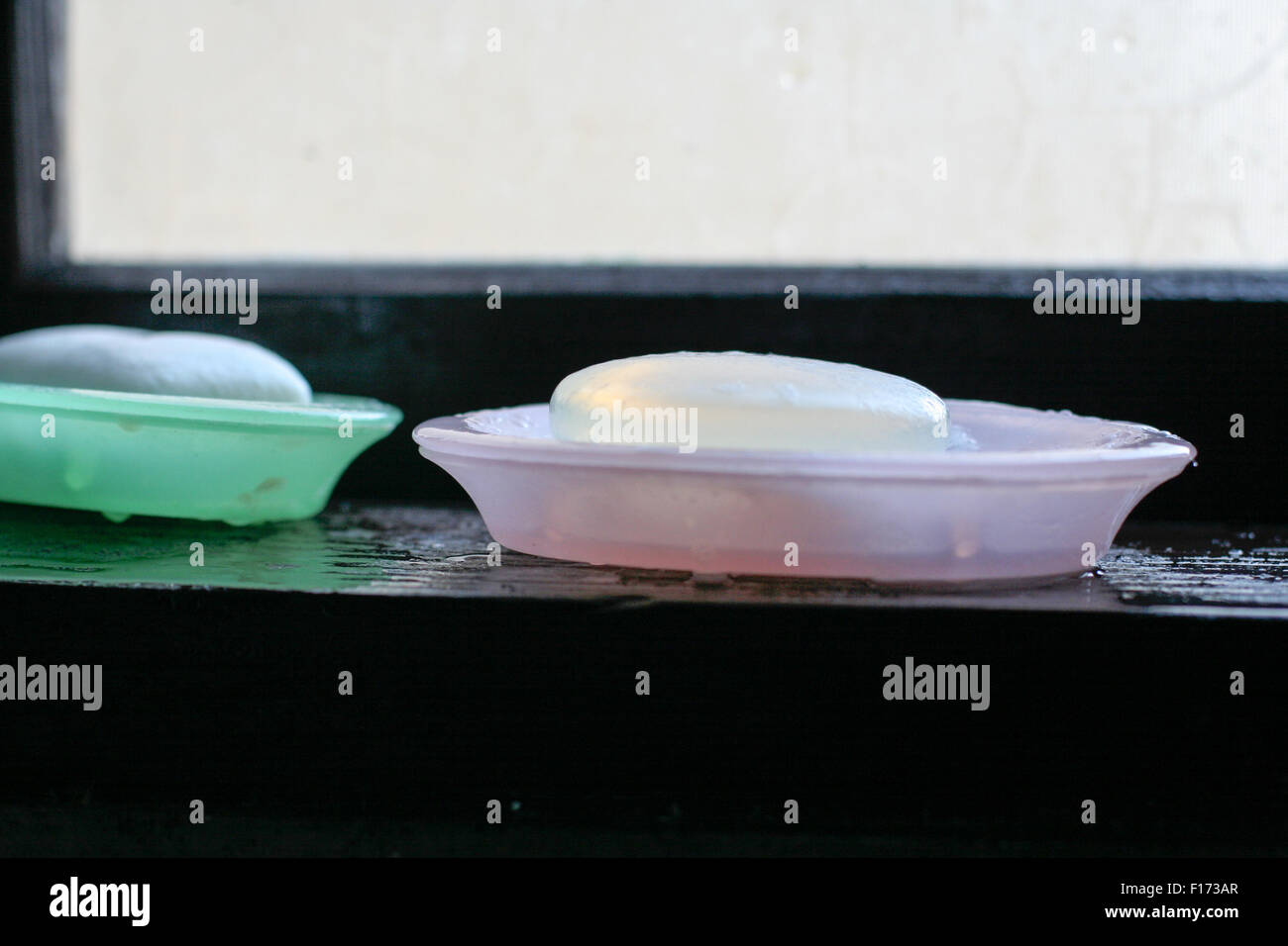 Two bars of glycerin soap sitting in two separate soap dishes pink and green on window sill