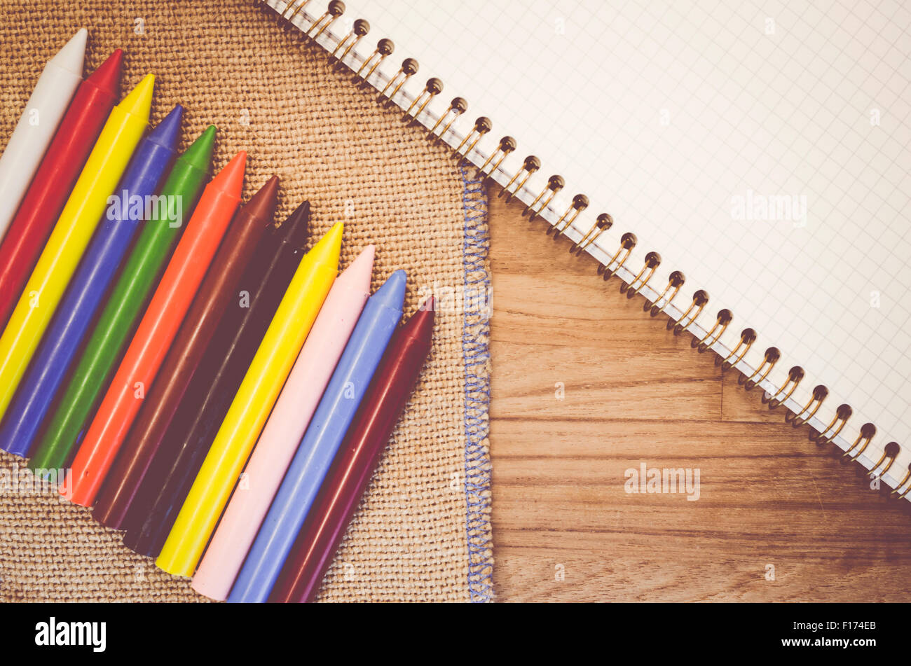 set of colored wax crayons and notebook on a natural burlap and wood ...